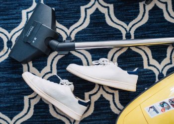 cleaning a dark blue carpet with a vacuum which is next to a pair of white shoes