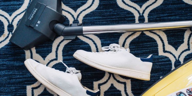 cleaning a dark blue carpet with a vacuum which is next to a pair of white shoes
