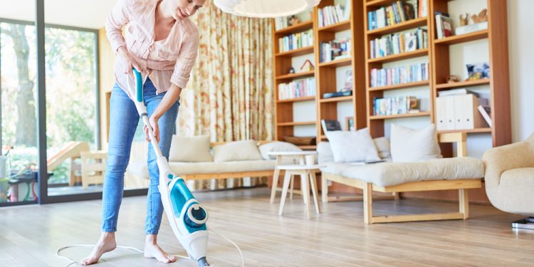 A woman is vacuuming the wooden floor of the study room