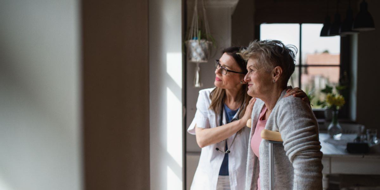 Side view of a healthcare worker or caregiver visiting senior woman indoors at home, helping her to walk.