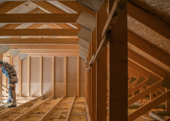 The Importance of Properly Insulating Your Attic Banner Image - Construction Worker Looking Downstairs. Attic Wooden Roof Construction. House Cover. Wooden Structure