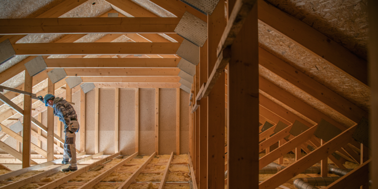 The Importance of Properly Insulating Your Attic Banner Image - Construction Worker Looking Downstairs. Attic Wooden Roof Construction. House Cover. Wooden Structure
