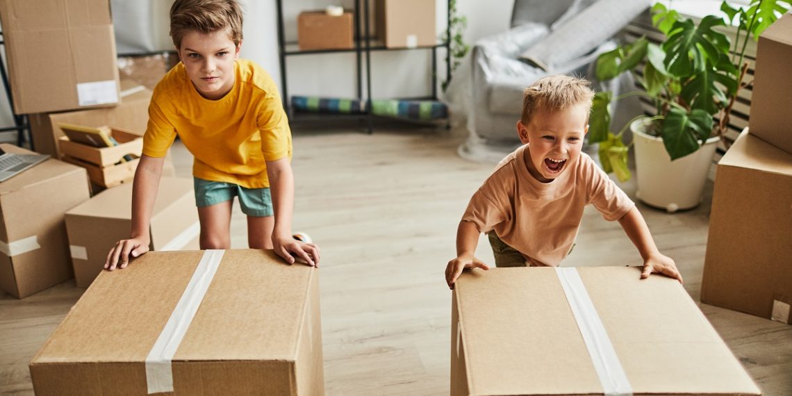Portrait of two boys moving cardboard boxes while family relocating to new house, copy space