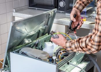People in technician jobs. Appliance repair technician or handyman works on broken dishwasher in a kittchen. Laborer is changing the heating element.