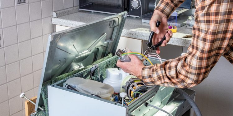 People in technician jobs. Appliance repair technician or handyman works on broken dishwasher in a kittchen. Laborer is changing the heating element.