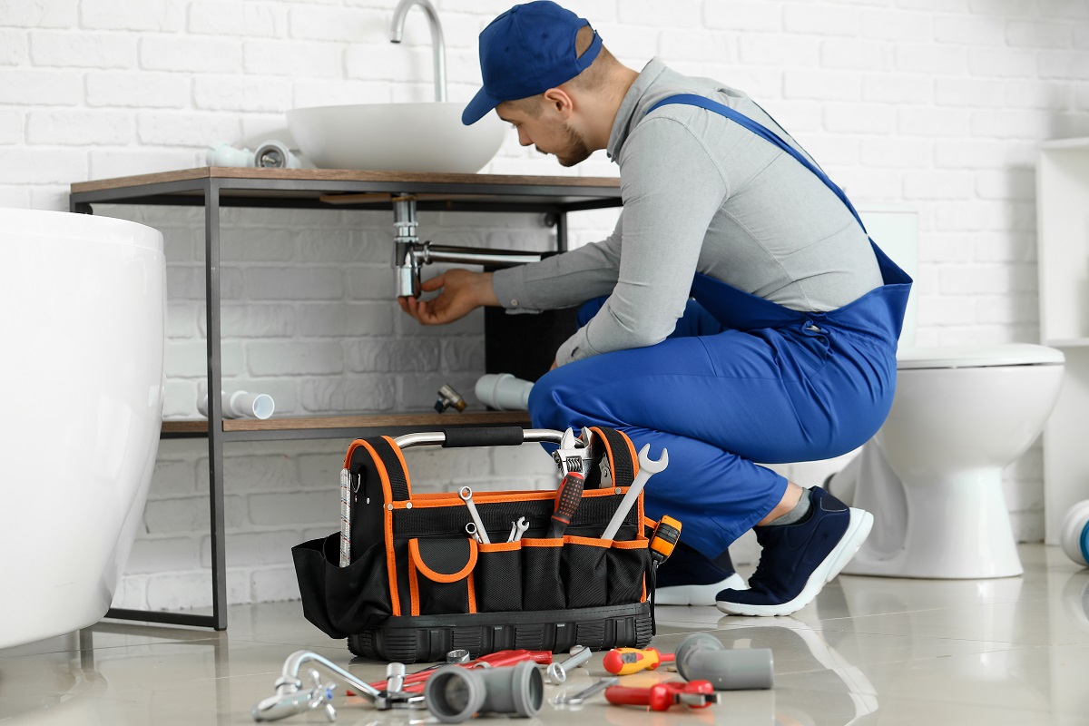 Handsome plumber repairing sink in bathroom