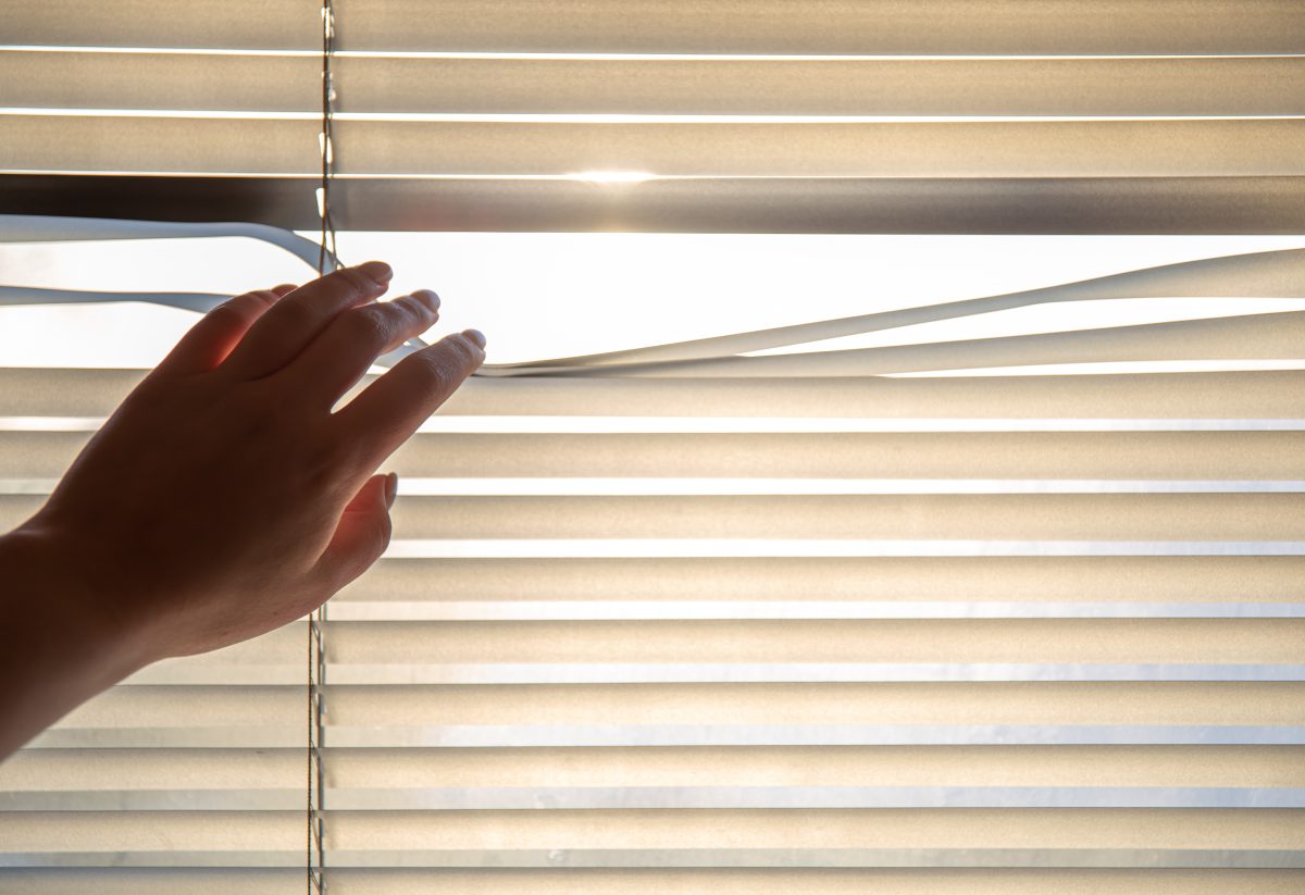 Windows venetian blinds, hand separating slats of venetian blinds with a finger to see through