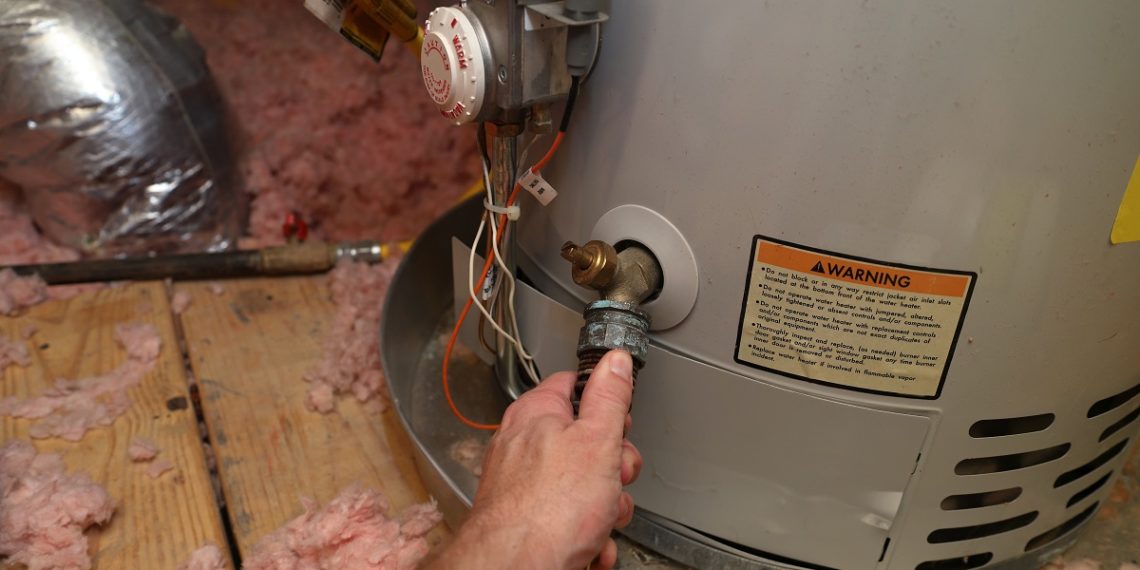 Hand attaches hose to a home water heater to perform maintenance