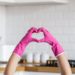 Heart made of pink protective gloves on white kitchen background.. Woman hands wearing protective gloves. Concept of clean kitchen, successful thumb up yes ok sign