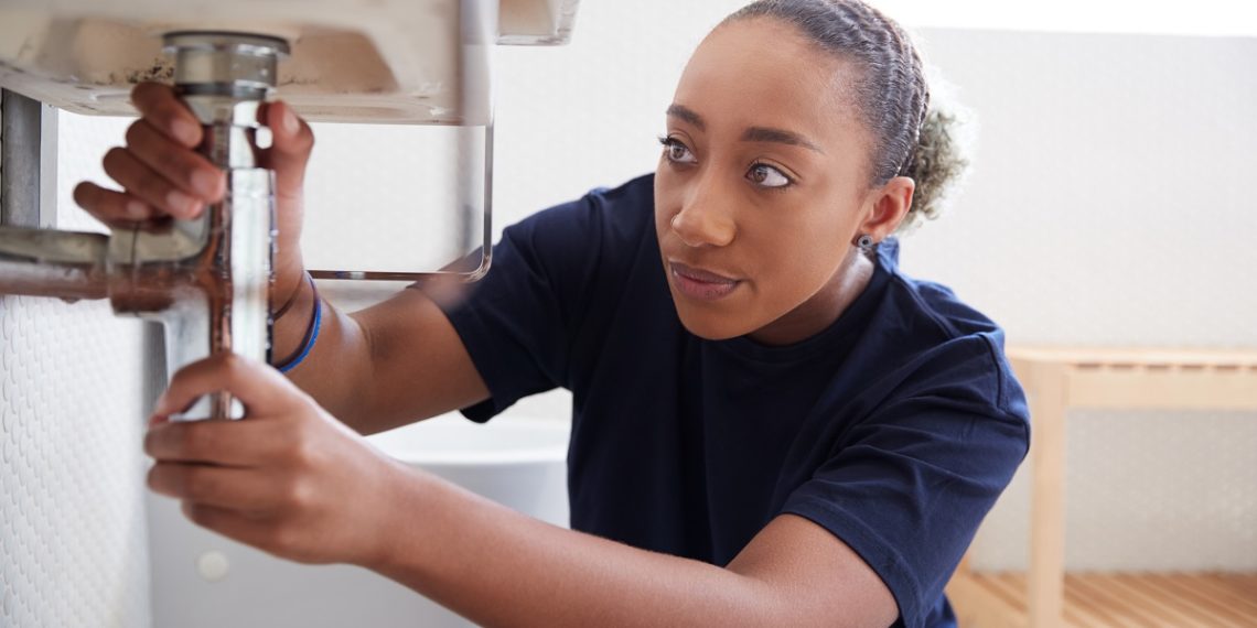 Female Plumber Working To Fix Leaking Sink In Home Bathroom