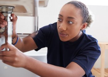Female Plumber Working To Fix Leaking Sink In Home Bathroom