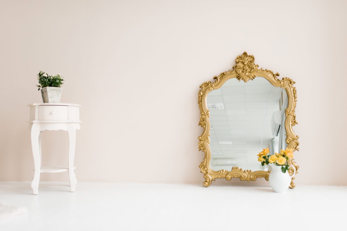 Mirror in a classic gold frame and potted flowers in the living room interior