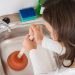 Happy Woman Using Plunger In Kitchen Sink At Home