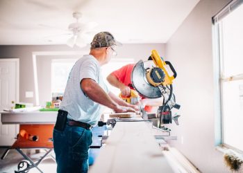 two men cutting wood with a circular saw in a white room