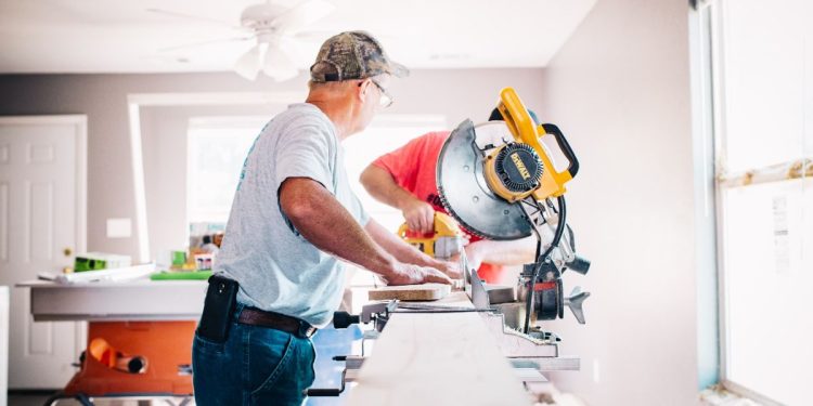 two men cutting wood with a circular saw in a white room
