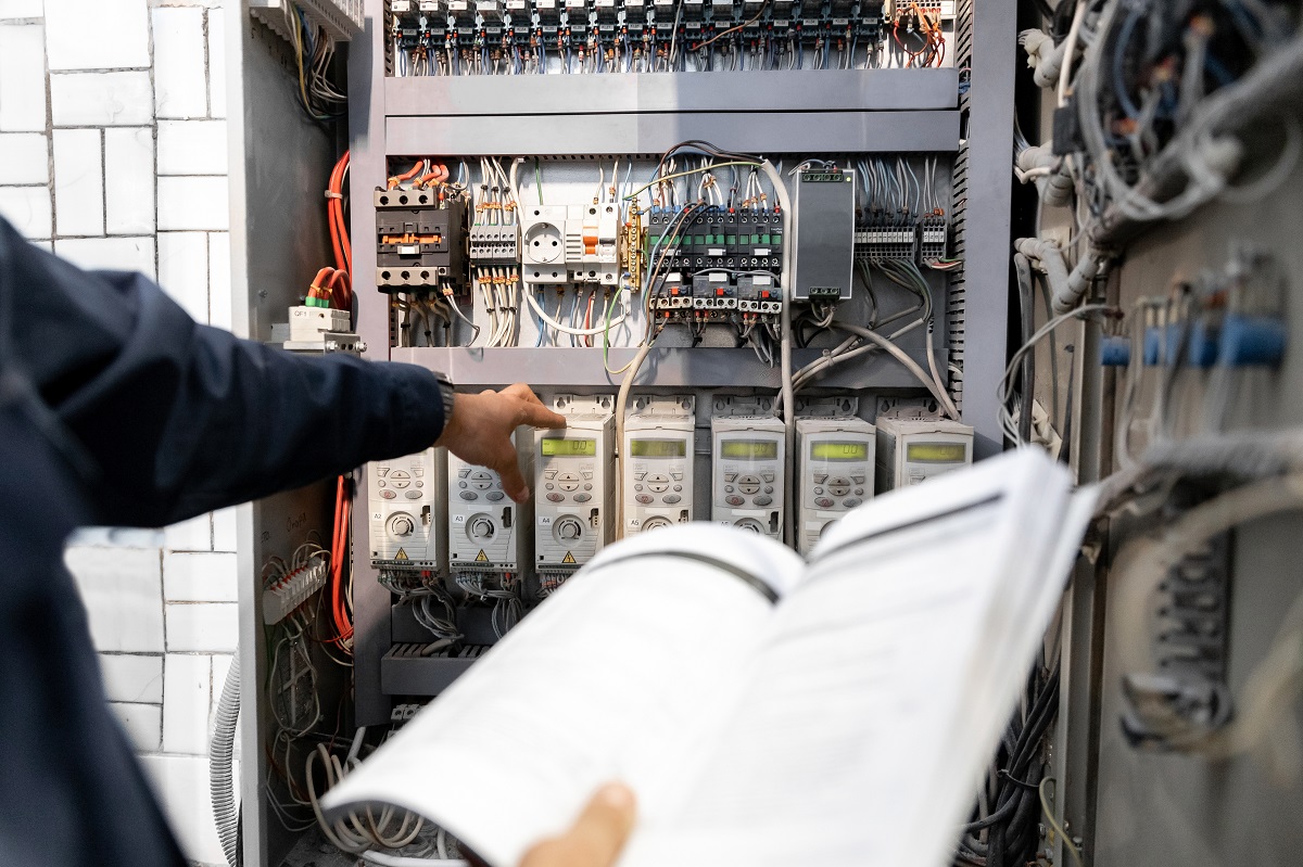 Worker engineer checks electrician measurements with tester multimeter for industrial production.