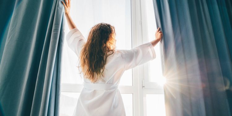 woman-opening-curtains-in-room-at-sunrise