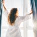 woman-opening-curtains-in-room-at-sunrise