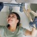 Cheerful young woman wearing protective gloves when fixing leaking sink pipe in kitchen