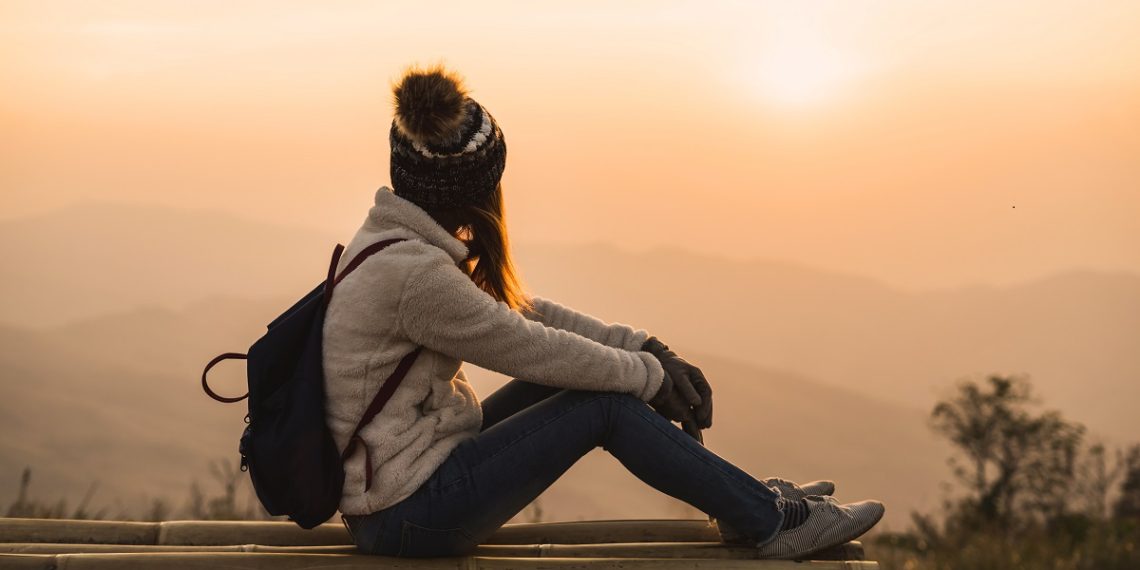 Young woman traveler looking at sunrise over the mountain